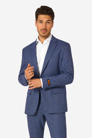 A men wearing a navy and blue checkered suit with a white dress shirt. The suit has a modern fit with two buttons and flap pockets. He stands against a plain white background.