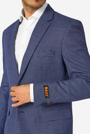 A men wearing a navy and blue checkered suit with a white dress shirt. The suit has a modern fit with two buttons and flap pockets. He stands against a plain white background. Close up of the chest