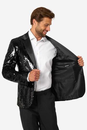Man in black sequin blazer holding the jacket open to reveal a smooth black inner lining with OppoSuits branding, smiling and looking down.