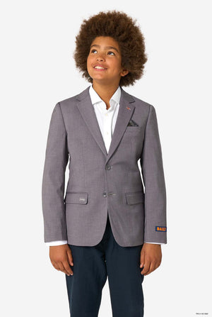 A child smiling while wearing a light grey blazer, white shirt, and dark trousers, looking upward.