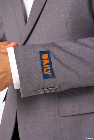 Close-up of a grey blazer sleeve showing a blue label with orange “DAILY” text and button details.