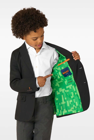 A boy showing the inside of a black blazer lined with green pixel-patterned fabric, pointing at the label.