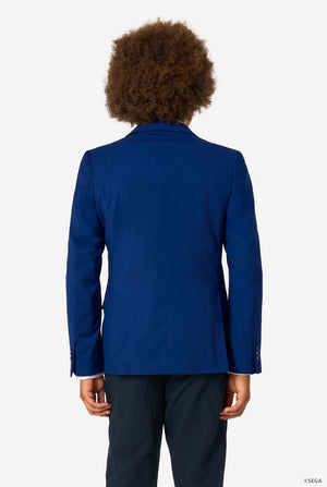 Back view of a child wearing a plain blue blazer and dark trousers, standing against a light background.