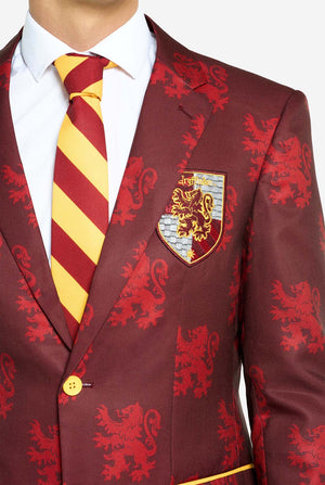 Image with light grey background and man wearing Harry Potter suit, Gryffindor styled. Suit consists of red blazer with Gryffindor logo and light red lions all over print, black pants, and red and yellow diagonal striped tie. Chest close up.