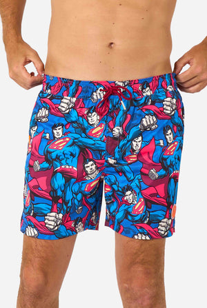 Man wearing a Men's Superman-themed swim shorts featuring a bold comic book design with multiple action poses of the Man of Steel. Perfect for superhero fans looking to make a splash. Close-up of his middle.