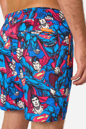Man wearing a Men's Superman-themed swim shorts featuring a bold comic book design with multiple action poses of the Man of Steel. Perfect for superhero fans looking to make a splash. Close up from the back.