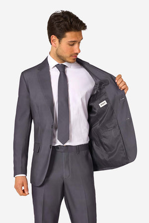 A man is wearing a stylish charcoal colored grey suit with a white dress shirt, looking confidently. Perfect formal outfit for men's special occasions, weddings, and parties. Holding one side of the jacket open.