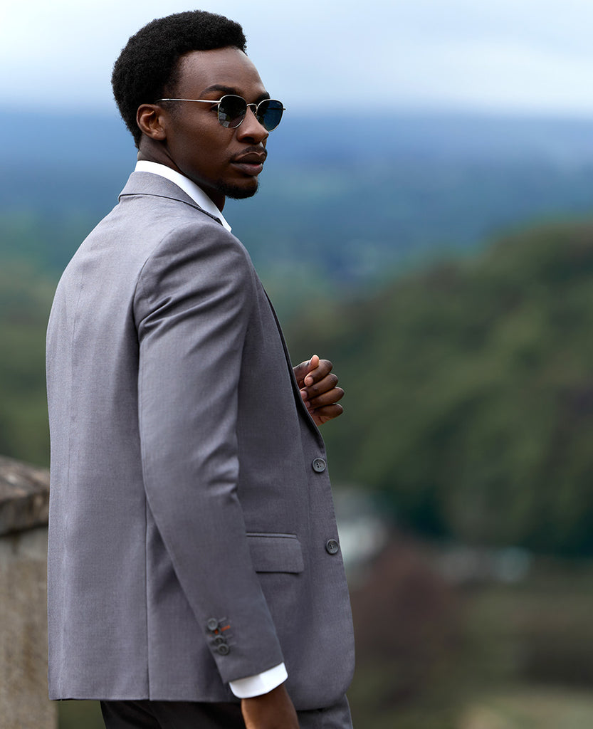 Man standing outside wearing dark grey suit, white shirt and sunglasses.