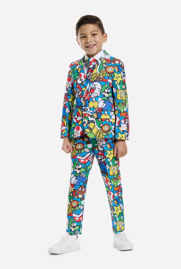 Image of kid wearing a Super Mario all over print suit, consisting of blazer, pants and tie. Main color is blue, but there is also yellow, red and white. Full body image.