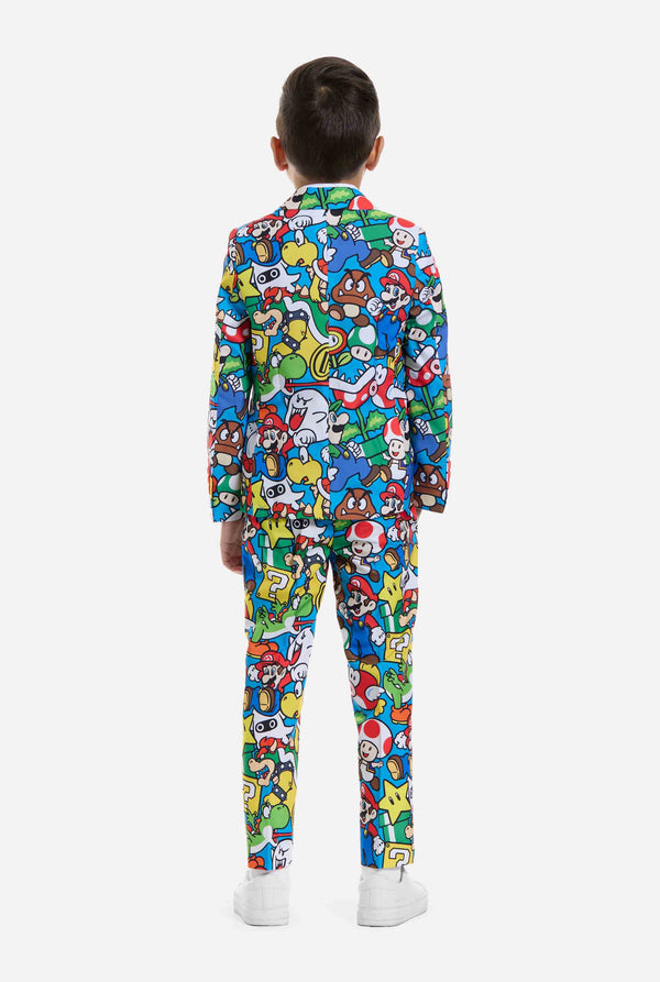 Image of kid wearing a Super Mario all over print suit, consisting of blazer, pants and tie. Main color is blue, but there is also yellow, red and white. View from the back.