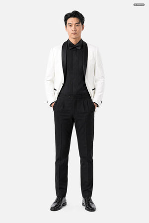 A man modeling a formal black and white tuxedo outfit, featuring a white blazer jacket with black lapels, a black pleated tuxedo shirt, a black bow tie, and black trousers, set against a plain light gray background.