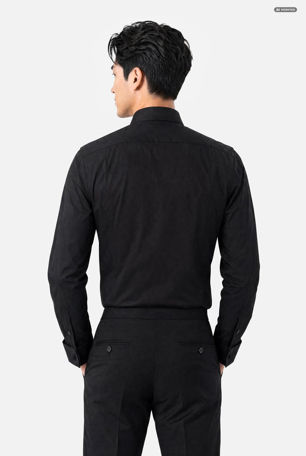A man viewed from the back wearing a black long-sleeve button-up shirt and black trousers against a light gray studio background.