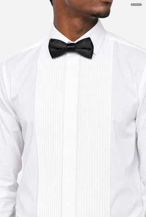 A close-up of a man wearing a white tuxedo shirt with a black bow tie, cropped from the lower face to the chest against a light gray background.