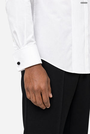 Close-up of a person wearing a white long-sleeve dress shirt with a buttoned cuff and black trousers, against a plain light background.