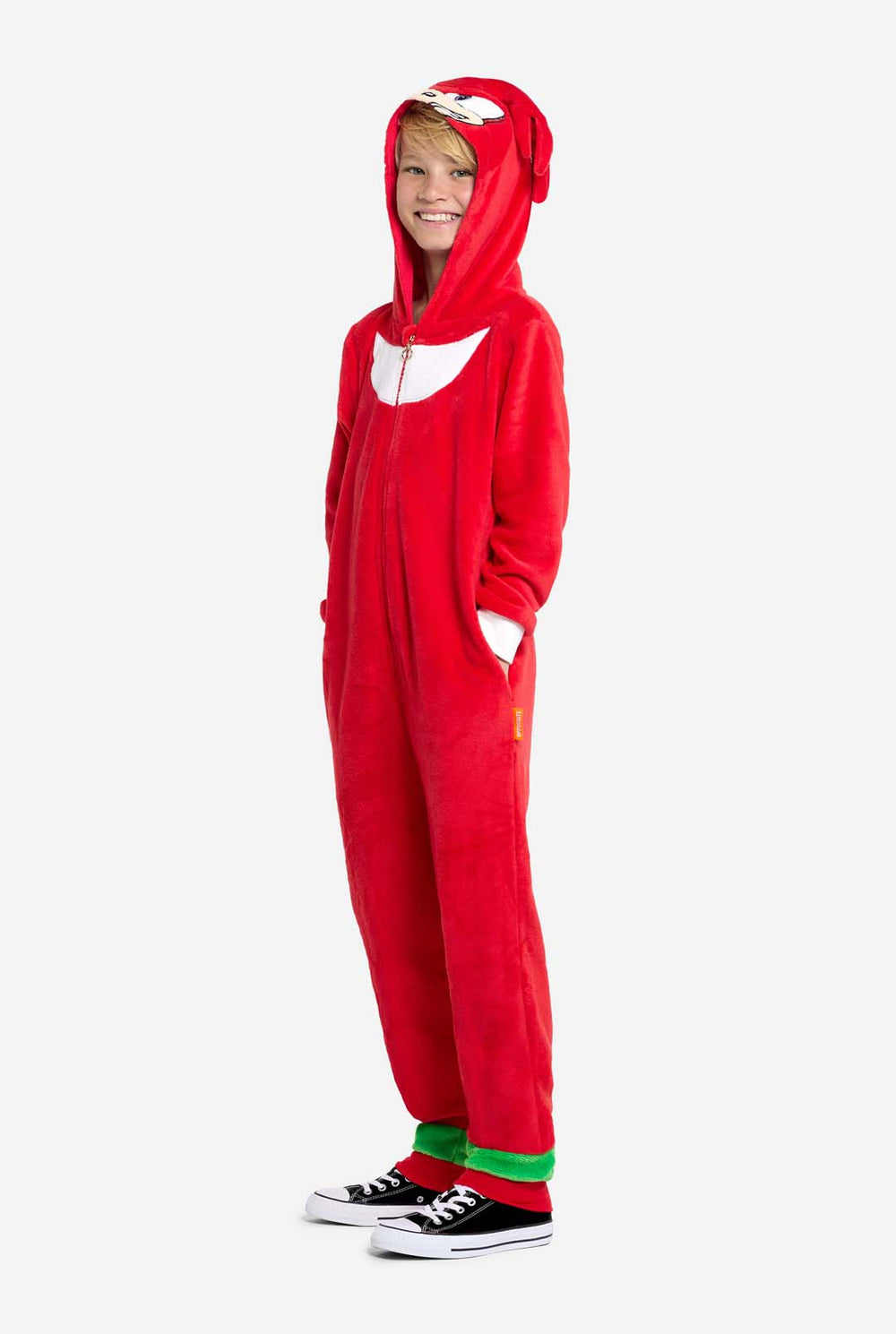 Smiling child standing front-facing, wearing a red Knuckles onesie with hood up and hands on hips. The onesie features a white chest patch and animated face on the hood.
