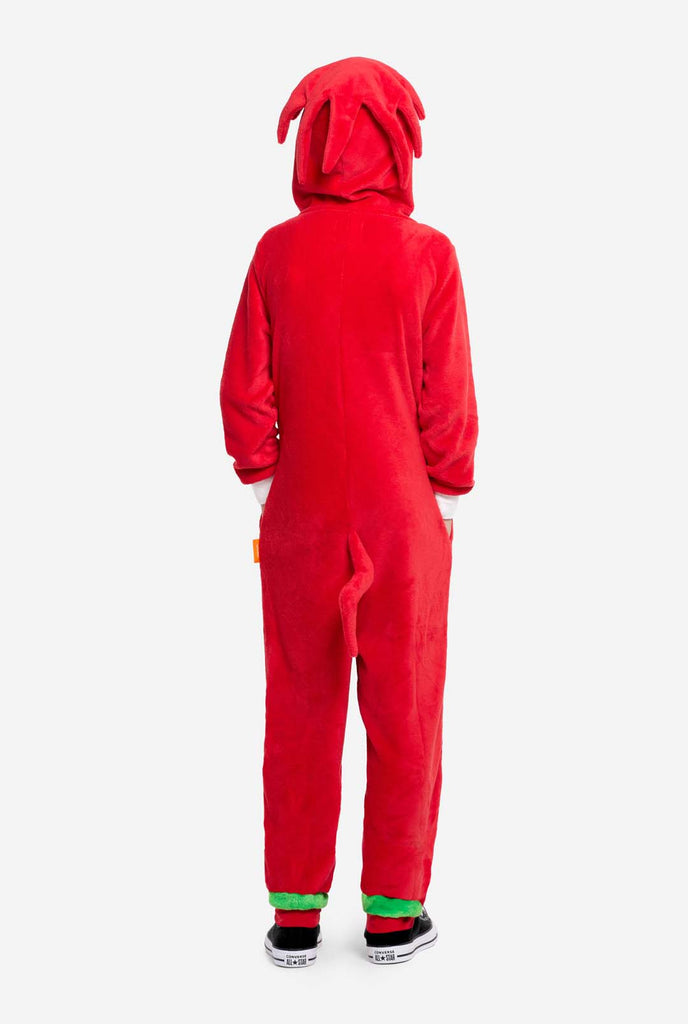 A kid is wearing a bright red Knuckles the Echidna-themed kids onesie from OppoSuits. The fun and cozy onesie features a zip-up front and an attached hood designed to resemble Knuckles' face, complete with expressive eyes and floppy dreadlocks. The suit is primarily red, with a white crescent pattern on the chest, reflecting Knuckles' iconic look from the Sonic the Hedgehog video game series. View from the back