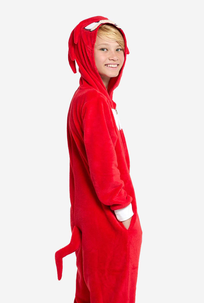 A kid is wearing a bright red Knuckles the Echidna-themed kids onesie from OppoSuits. The fun and cozy onesie features a zip-up front and an attached hood designed to resemble Knuckles' face, complete with expressive eyes and floppy dreadlocks. The suit is primarily red, with a white crescent pattern on the chest, reflecting Knuckles' iconic look from the Sonic the Hedgehog video game series. Side view.