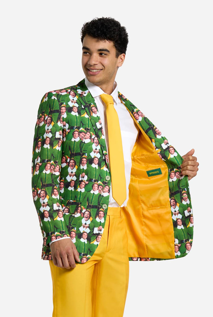 Man wearing men's Christmas suit with the character ELF on the jacket and yellow pants. Suits consists of all over print jacket with ELF Christmas movie character, yellow pants and yellow tie. Man also wearing a white shirt. Holding one side of the jacket open, showing yellow lining.