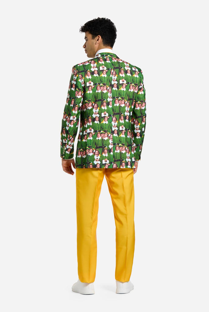 Man wearing men's Christmas suit with the character ELF on the jacket and yellow pants. Suits consists of all over print jacket with ELF Christmas movie character, yellow pants and yellow tie. Man also wearing a white shirt and white sneakers. View from the back.