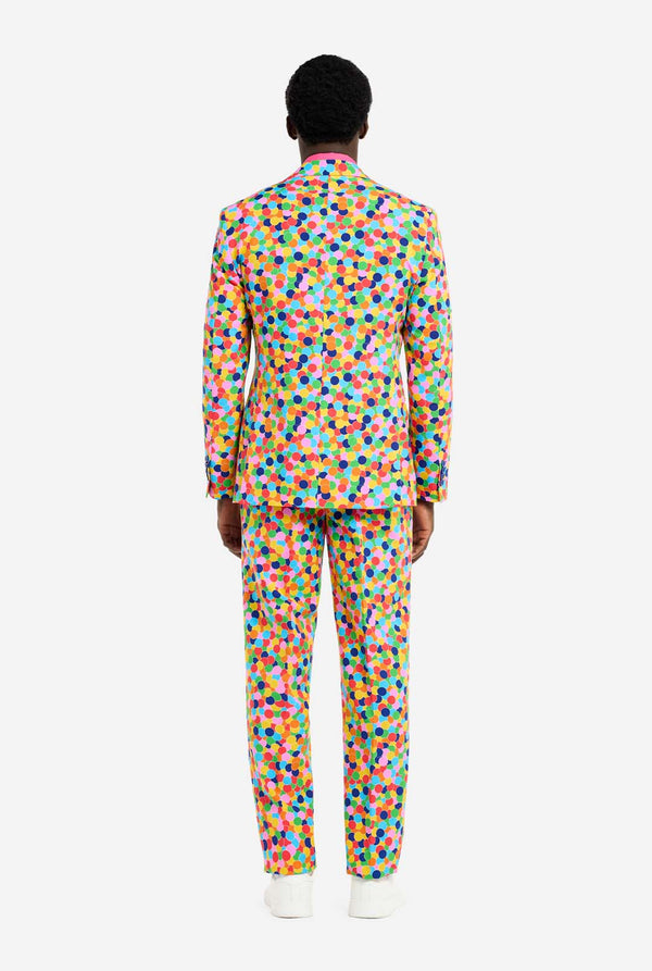 Man wearing men's suit with multicolor all-over confetti print and pink dress shirt. Suit consist of jacket, pants and tie. View from the back.
