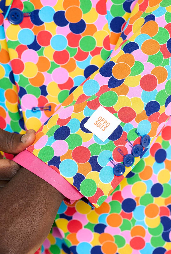 Man wearing men's suit with multicolor all-over confetti print and pink dress shirt. Suit consist of jacket, pants and tie. Sleeve close-up.