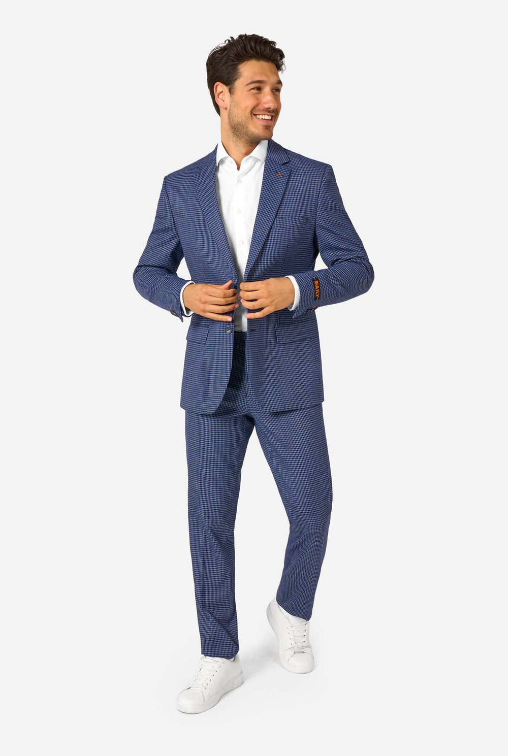 A men wearing a navy and blue checkered suit with a white dress shirt. The suit has a modern fit with two buttons and flap pockets. He stands against a plain white background.