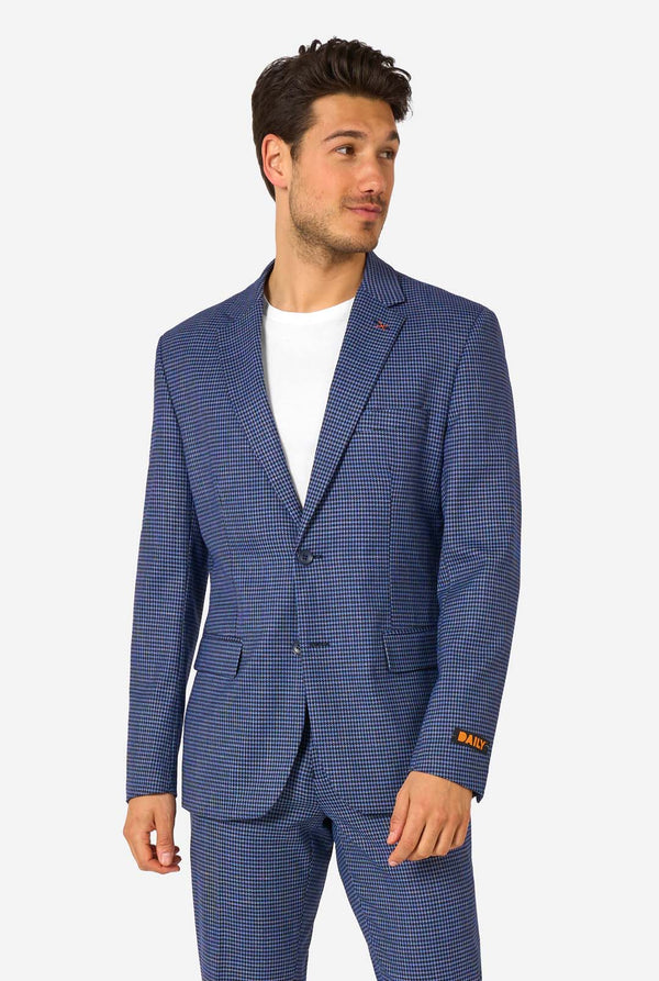 A men wearing a navy and blue checkered suit with a white dress shirt. The suit has a modern fit with two buttons and flap pockets. He stands against a plain white background.
