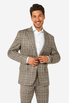 A men wearing a tan checkered suit with a white dress shirt. The suit has a modern fit with two buttons and flap pockets. He stands against a plain white background.