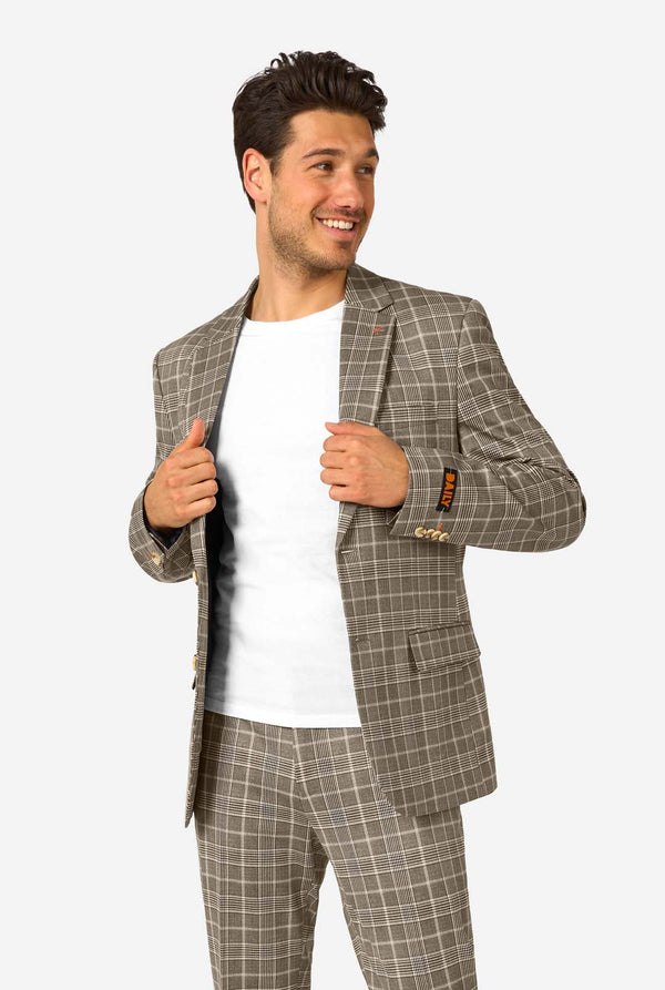 A men wearing a tan checkered suit with a white dress shirt. The suit has a modern fit with two buttons and flap pockets. He stands against a plain white background. 