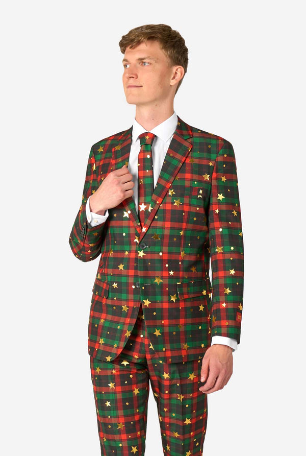Man wearing a red and green tartan plaid suit with gold star and dot accents, standing with one hand adjusting his matching tie.