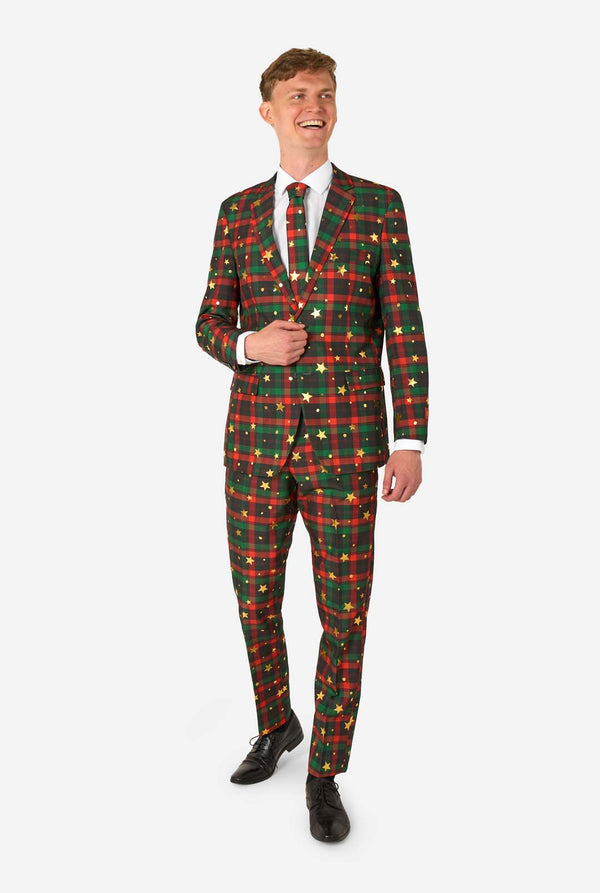Man in a red and green tartan plaid suit with gold star and dot accents, smiling while standing with one hand near his jacket button.