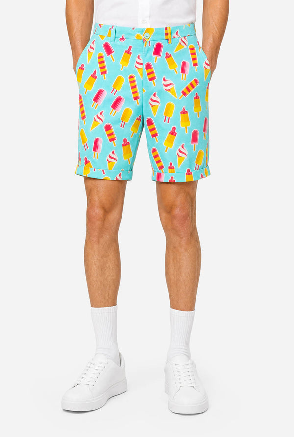 Man wearing light blue summer suit with ice cream and ice loly print. Suits consists of shorts, short sleeved blazer and tie. Pants view.