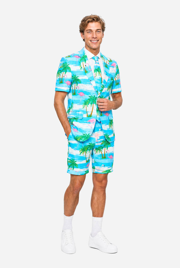 Man wearing a colorful tropical-themed suit, with palm trees and pink flamingos on a light background. Full body image.