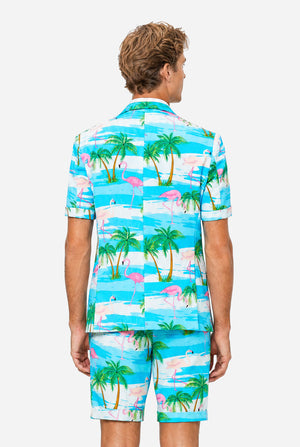 Man wearing a colorful tropical-themed suit, with palm trees and pink flamingos on a light background. View from the back.