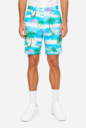 Man wearing a colorful tropical-themed short, with palm trees and pink flamingos on a light background.
