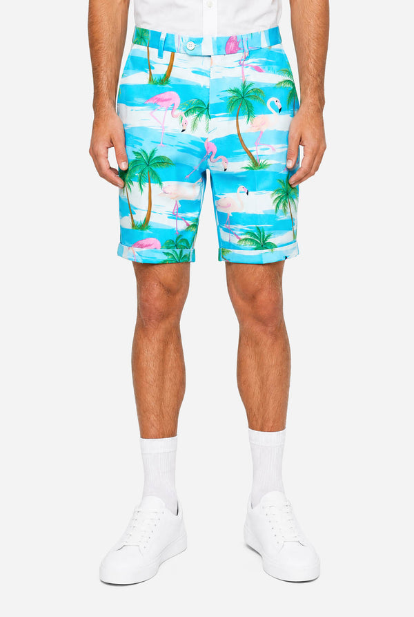 Man wearing a colorful tropical-themed short, with palm trees and pink flamingos on a light background.