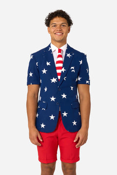 Person wearing a blue blazer with white star patterns, white shirt, and red shorts on a white background