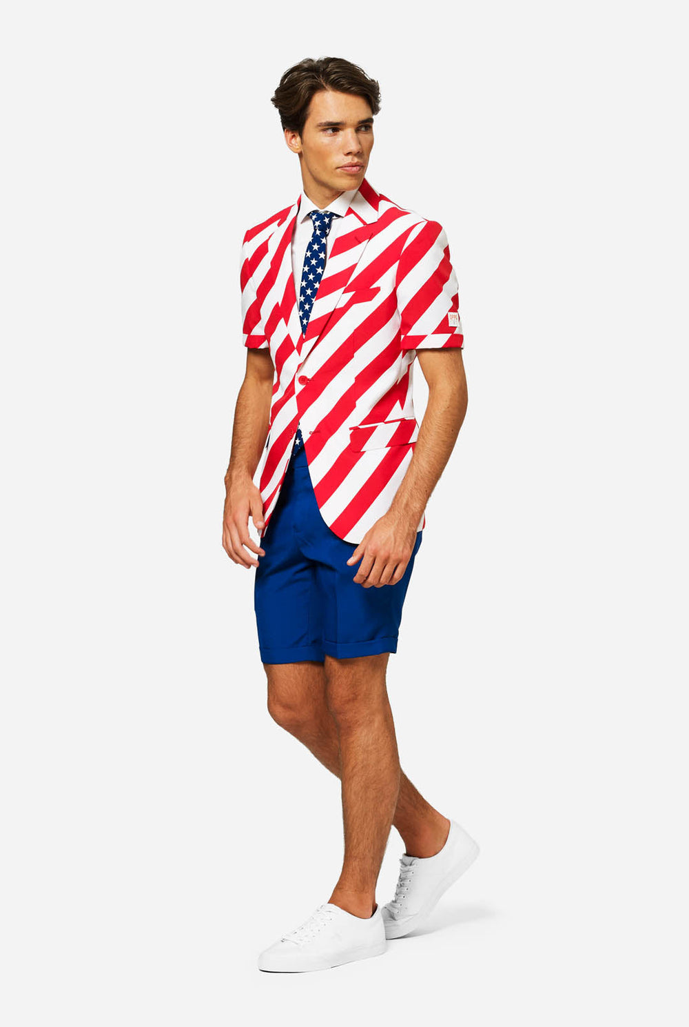 Man wearing a red and white, striped blazer and blue shorts with an American flag pattern on a plain background