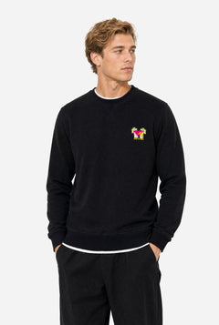 Man wearing a black crewneck sweatshirt against a light gray background, featuring a MTV logo embroidery in Pink and yellow on the left chest.