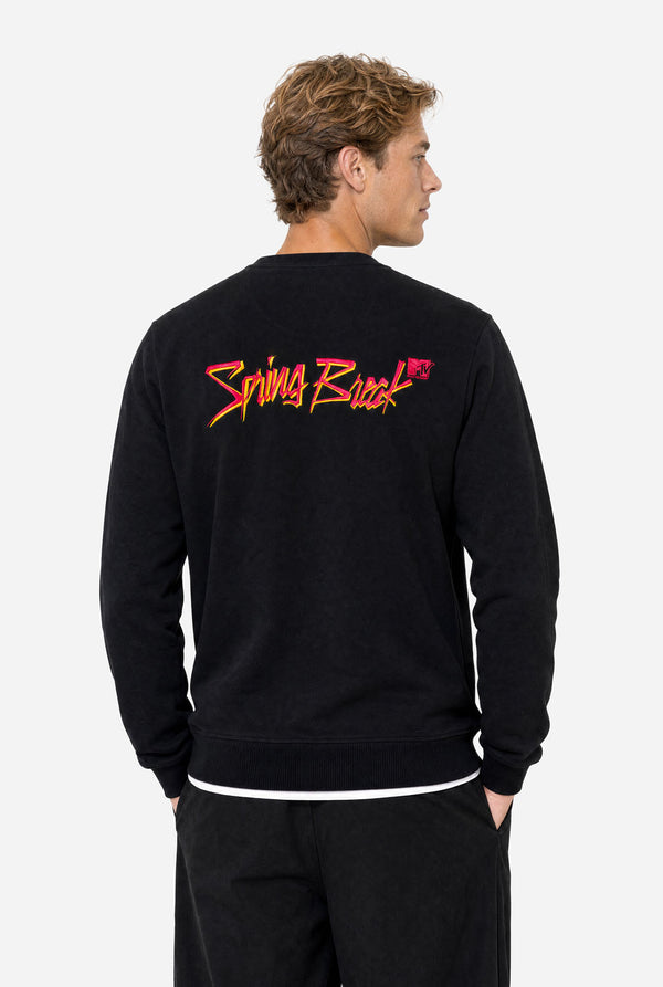 Man wearing a black crewneck sweatshirt against a light gray background, featuring a stylized 'Spring Break and MTV logo embroidery in Pink and yellow across the upper back.