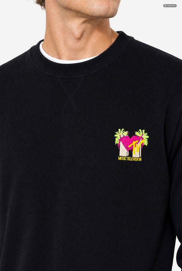 A close-up of a person wearing a black crewneck sweatshirt with a colorful embroidered MTV graphic on the left chest. 