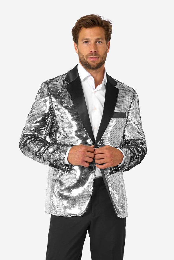 Man wearing a silver sequin blazer with black satin lapel, buttoning the jacket while standing against a plain background.