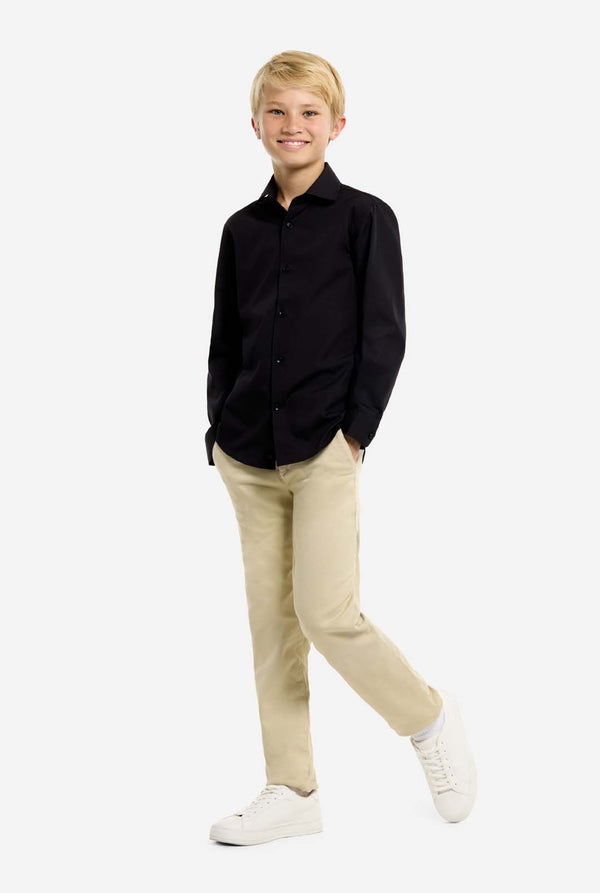 Boy is wearing a black shirt, beige pants, and white shoes on a white background. Full body image.