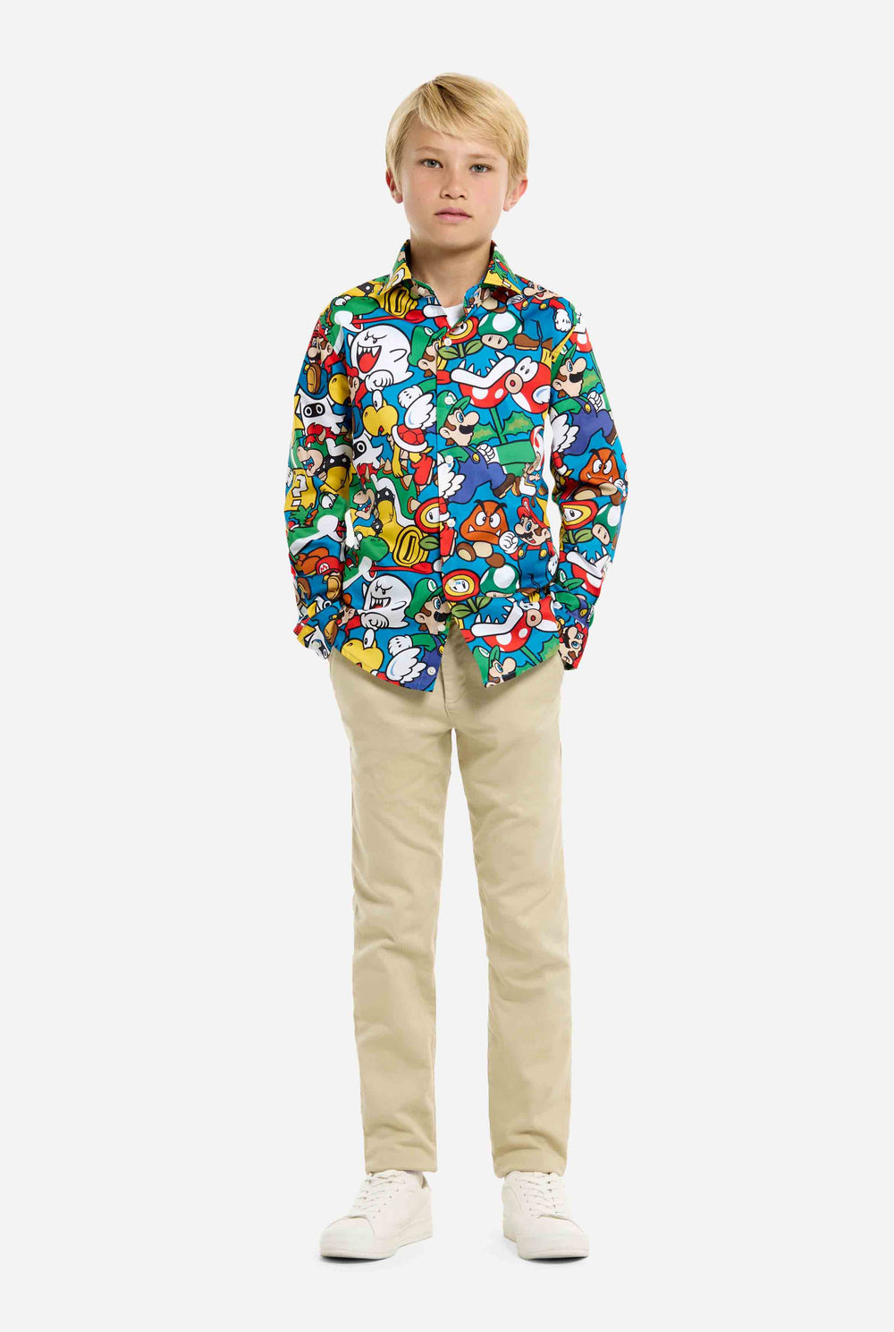 Image of teen wearing a Super Mario all over print shirt. Main color is blue, but there is also yellow, red and white. He has his hands in his pockets.