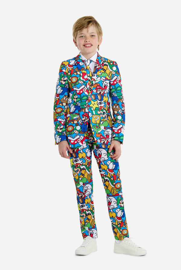 Image of teen wearing a Super Mario all over print shirt, consisting of blazer, pants and tie. Main color is blue, but there is also yellow, red and white. Full body image.