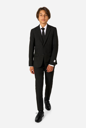 Teenager wearing a black suit and a white shirt on a light background. Full body image.