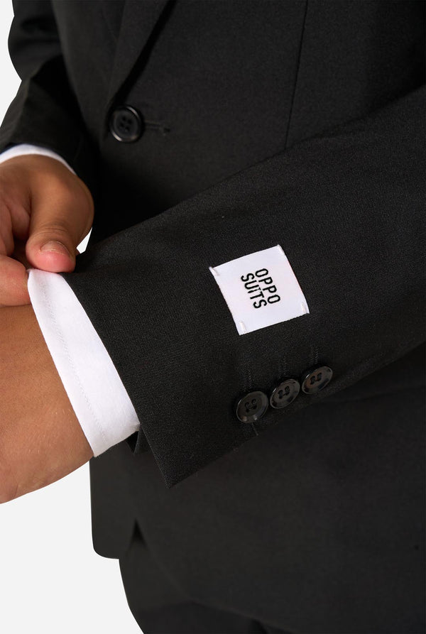 Teenager wearing a black suit and a white shirt on a light background. Sleeve close up.