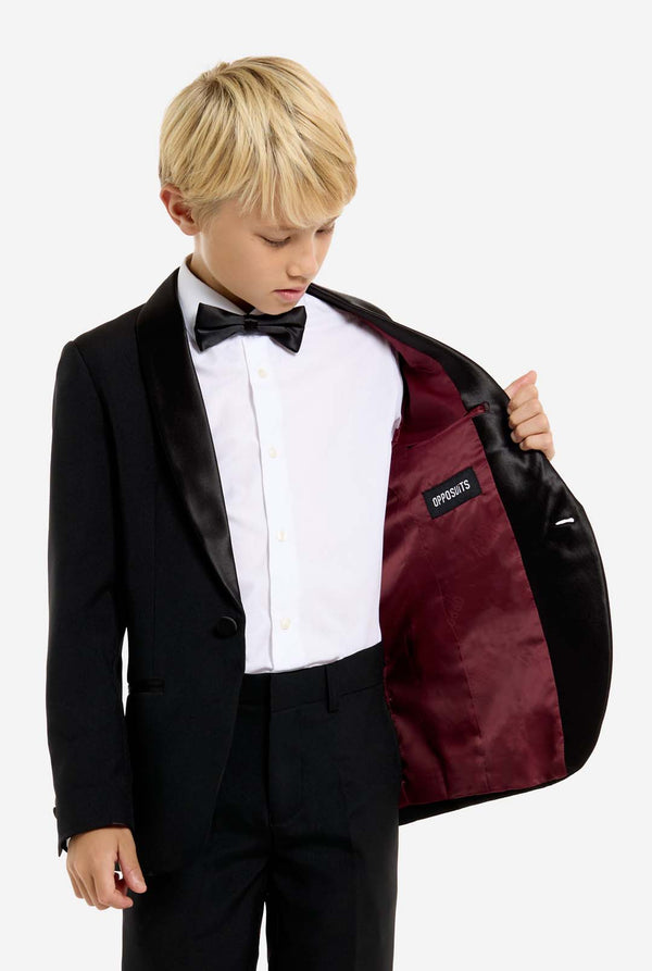Young boy in a black tuxedo with a white shirt and black bow tie, holding a matching jacket.