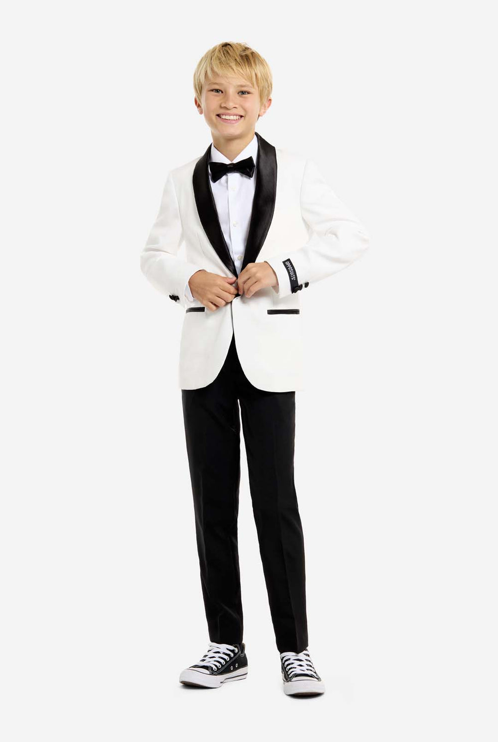 Young boy wearing a white tuxedo with black bow tie and pants on a white background