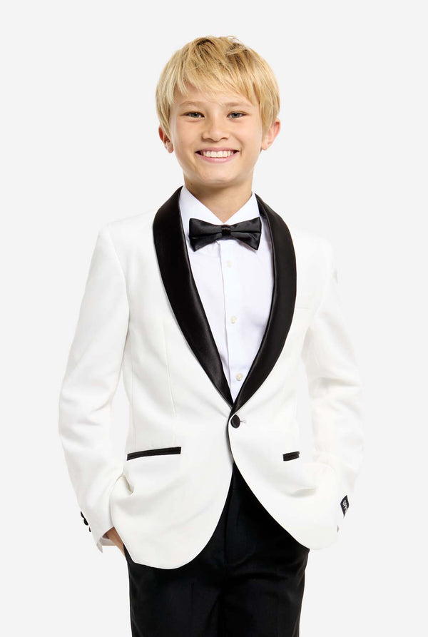 Person wearing a white tuxedo with black bow tie and pants on a white background. Hands in the pockets.